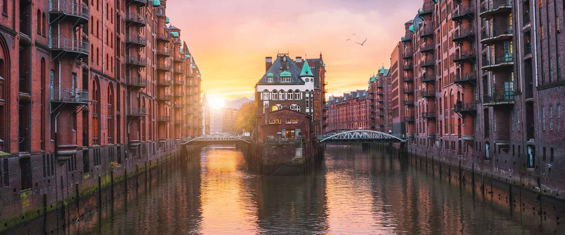 View of the port in Berlin at sunset, surrounded by historic brick buildings, with a boat on the water and a warm, orange sky.