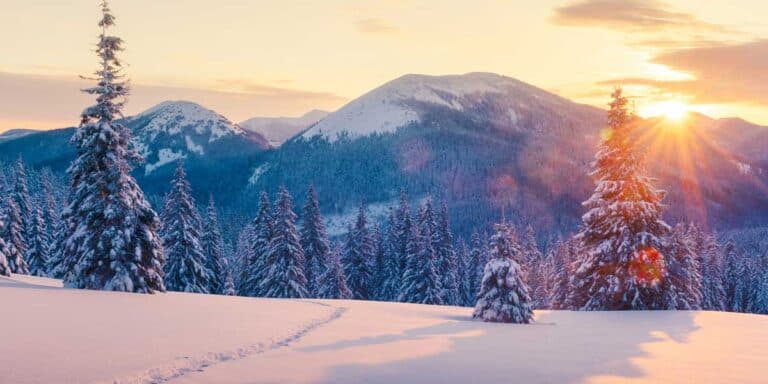 Hübsche Escort Lady in winterlicher Berglandschaft bei Sonnenuntergang, Luxus Escort Service, exklusive Begleitung in verschneiter Natur.