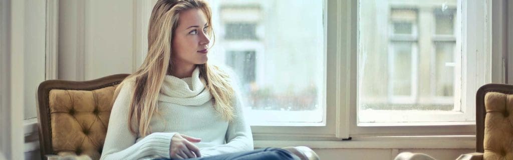 A seductive escort sits by the window, enjoying the view, awaiting her in a comfortable setting. An elegant companion for private occasions, combining discretion and charm.