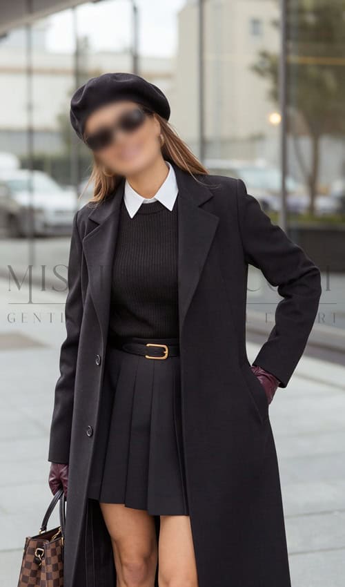 Stilvolle Escort Dame Joana in urbaner Umgebung, trägt schwarze Kleidung, Hut und trägt eine Handtasche, perfekt für diskrete Begleitung.
